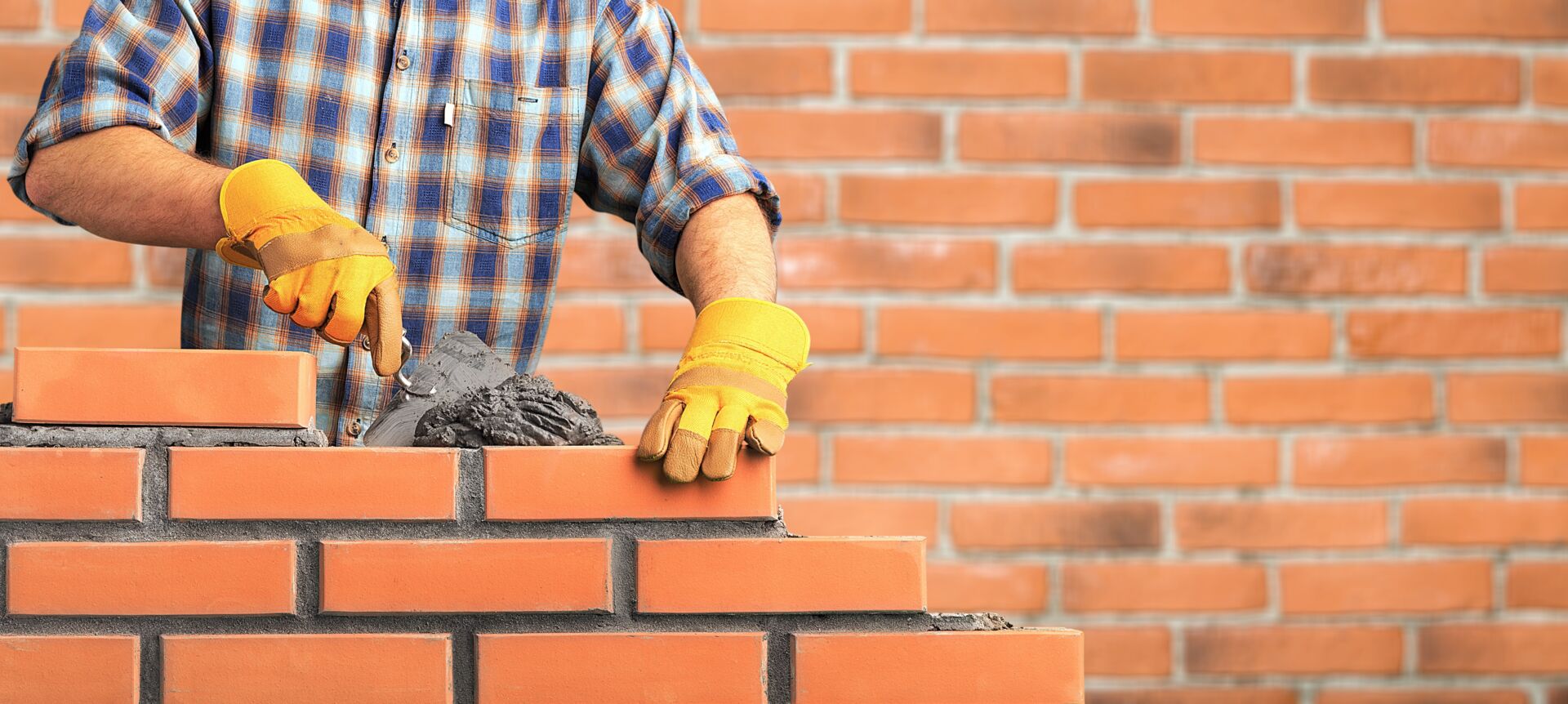 Ein Maurer mit gelben Handschuhen bearbeitet eine Ziegelwand, im Kontext der Hans Müller GmbH.